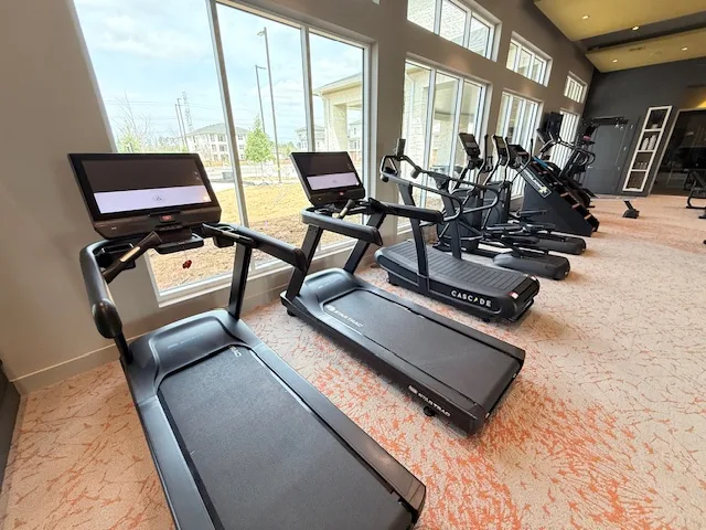 Star Trac touchscreen treadmills and a curved runner along tall windows in a Spring, Texas apartment gym