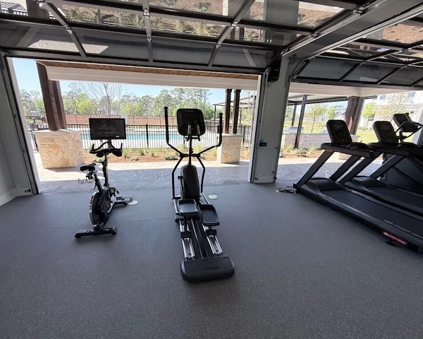 Indoor cycle and elliptical at an open glass roll-up door onto the pool in a Spring, Texas apartment gym