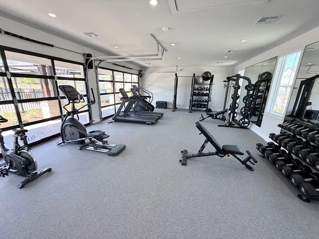 Apartment gym with glass roll-up doors, ellipticals, treadmills, a bench and dumbbell rack in Spring, Texas