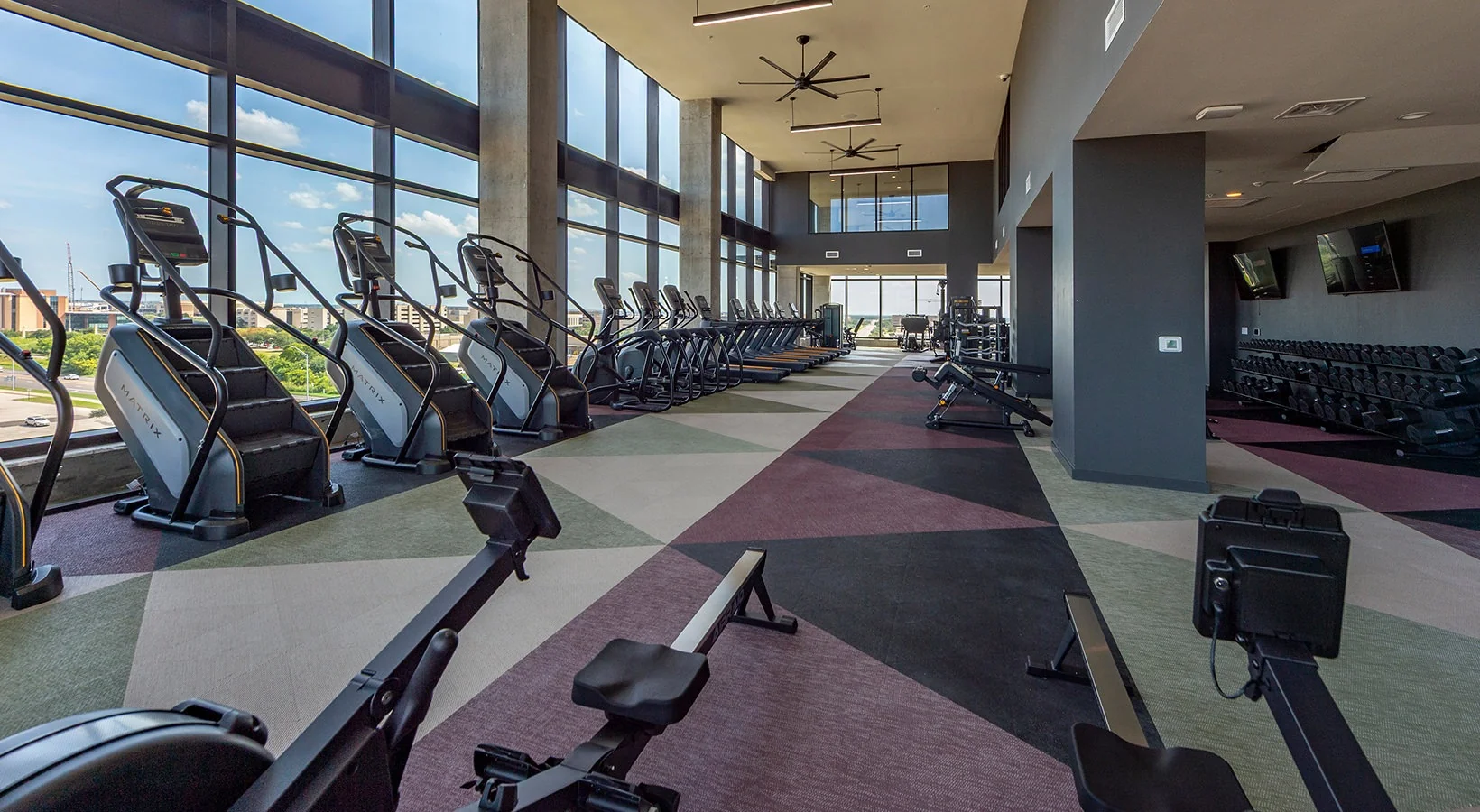 Glass-walled cardio room in a Texas student housing tower with Matrix stair climbers, treadmills and a dumbbell rack