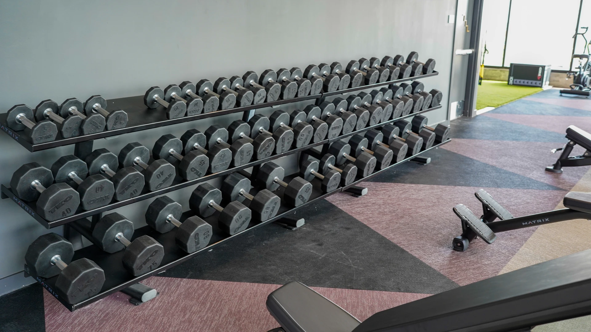 Extensive wall-mounted dumbbell rack spanning a student housing fitness center strength floor