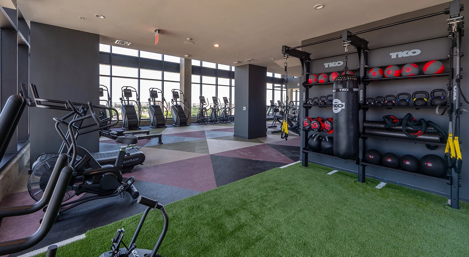Turf functional zone in a student housing wellness center with a TKO storage wall, heavy bag and AirRaid bike