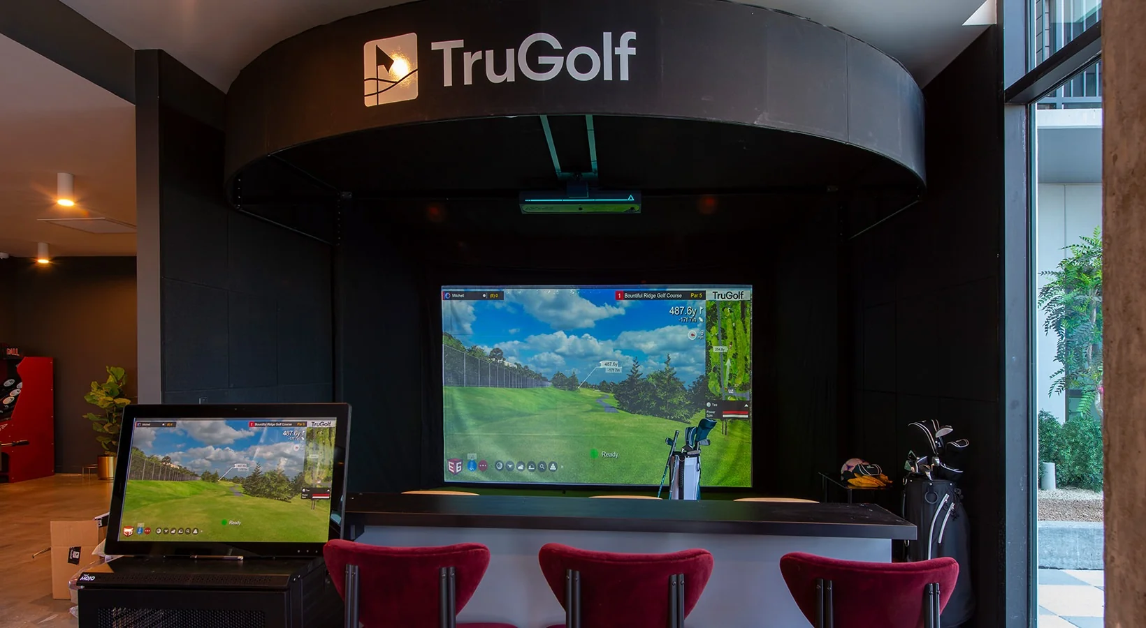 Golf simulator lounge in a student housing gameroom with a large projection screen and bar seating