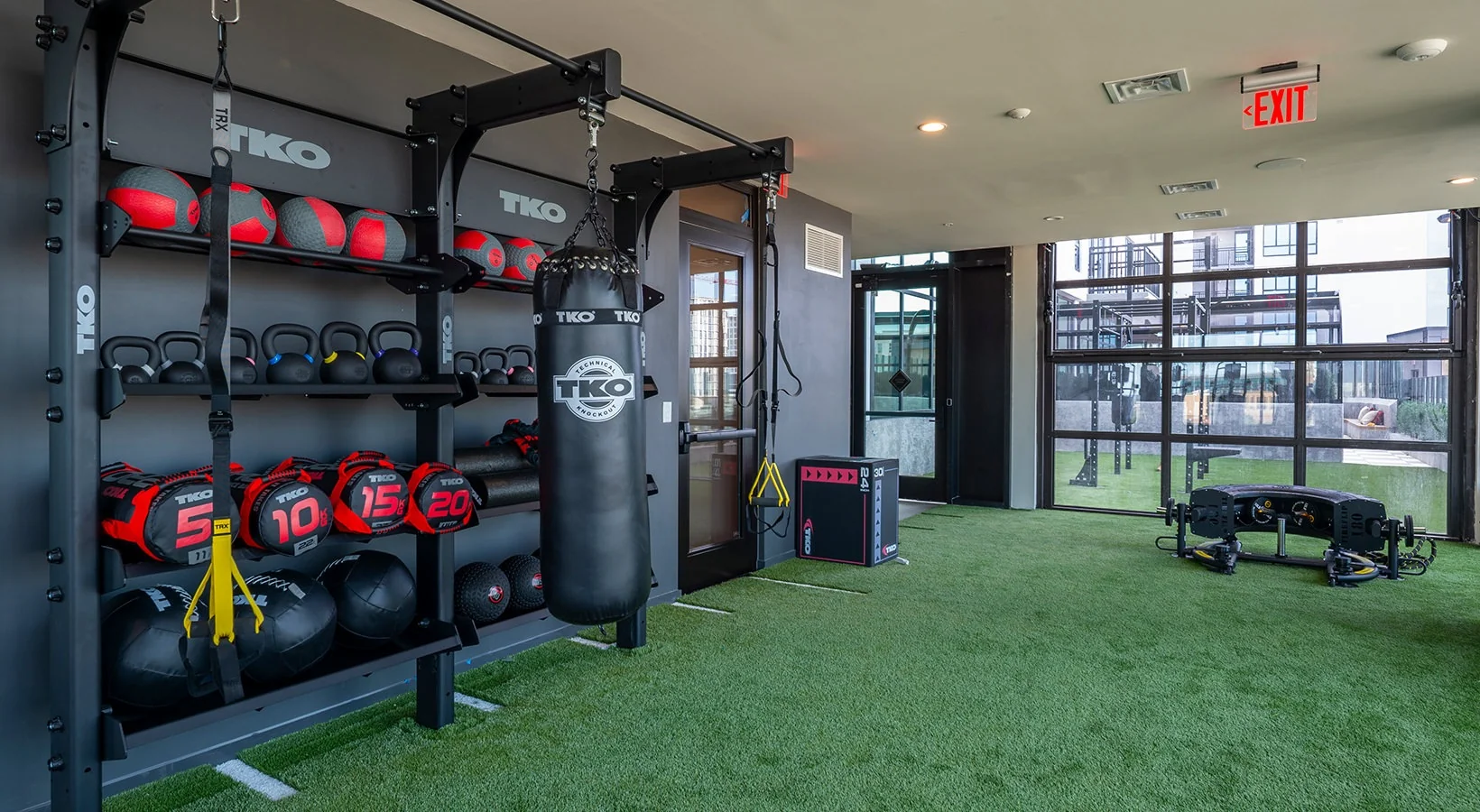 Indoor functional training wall opening through a garage door onto an outdoor turf training deck at a student housing tower