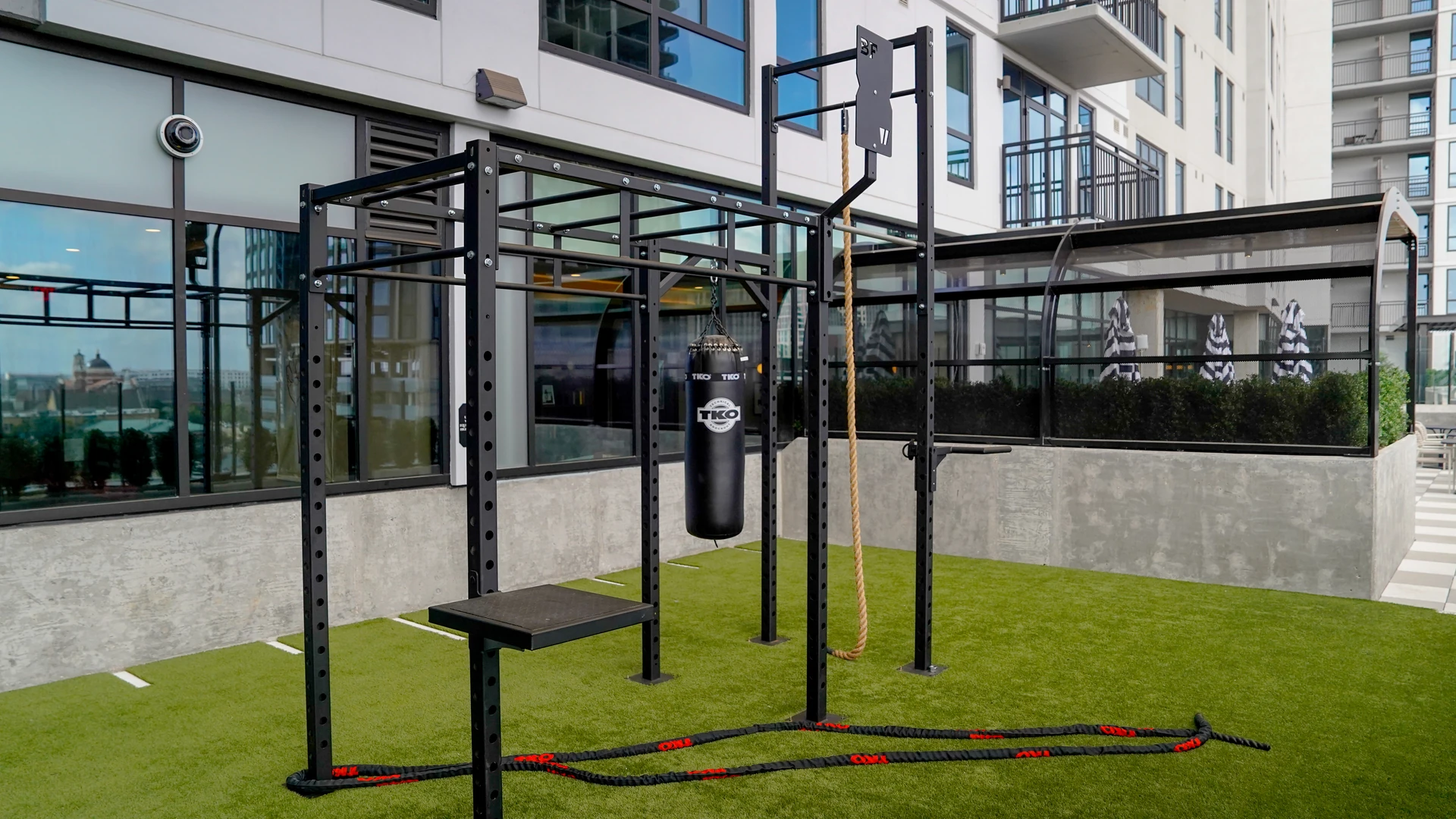 BeaverFit outdoor rig with a TKO heavy bag and climbing rope on a rooftop turf deck, skyline behind it