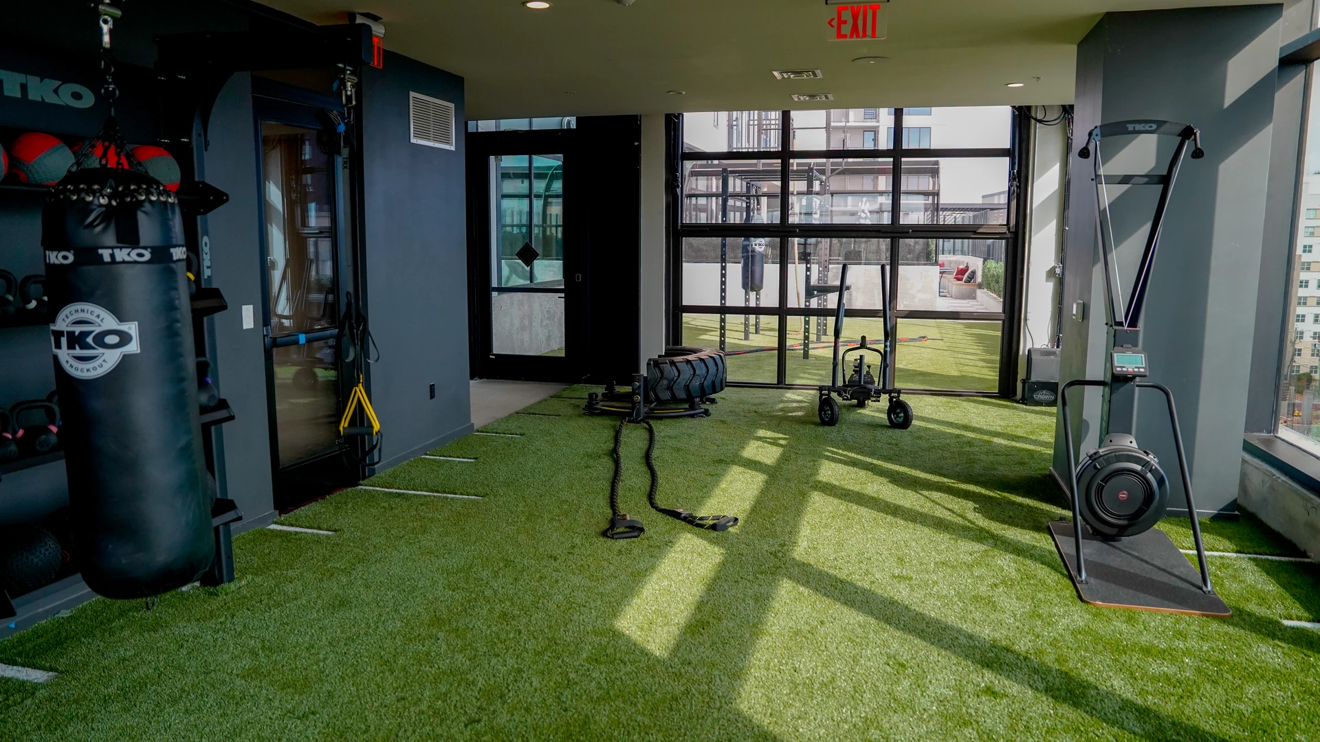 Wide view of a rooftop turf training deck with an outdoor rig, heavy bag and climbing rope