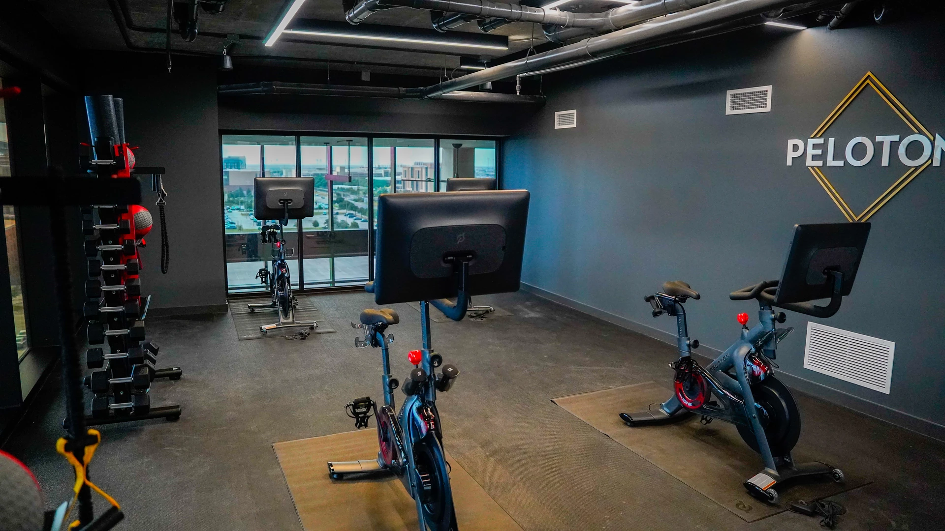 Peloton-branded studio with connected bikes facing floor-to-ceiling windows and a city skyline