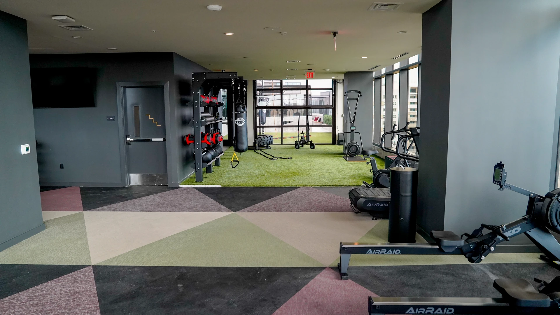 TKO wall rack of heavy bags and medicine balls beside a glass door onto an outdoor turf deck