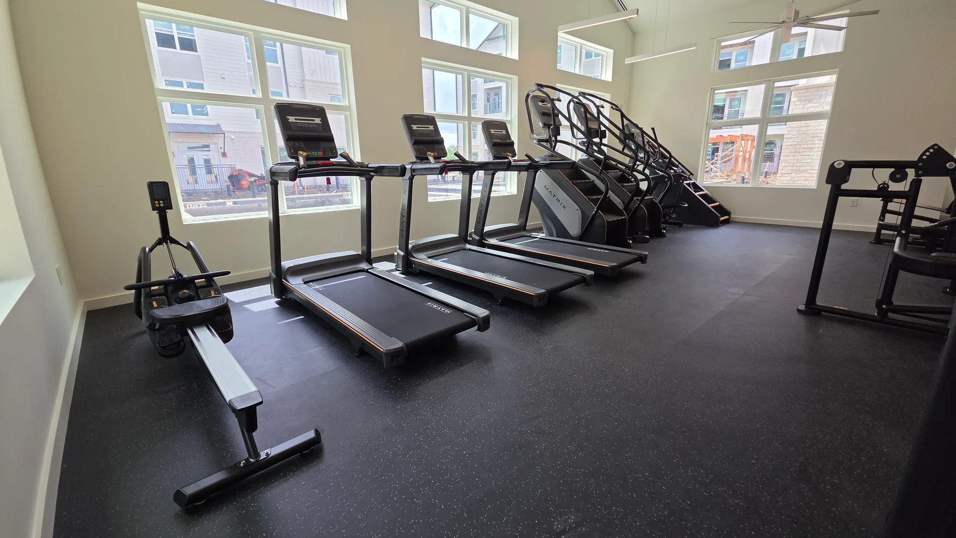 Matrix treadmills, a rower and a Jacob's Ladder along tall windows in a Webster, Texas apartment gym