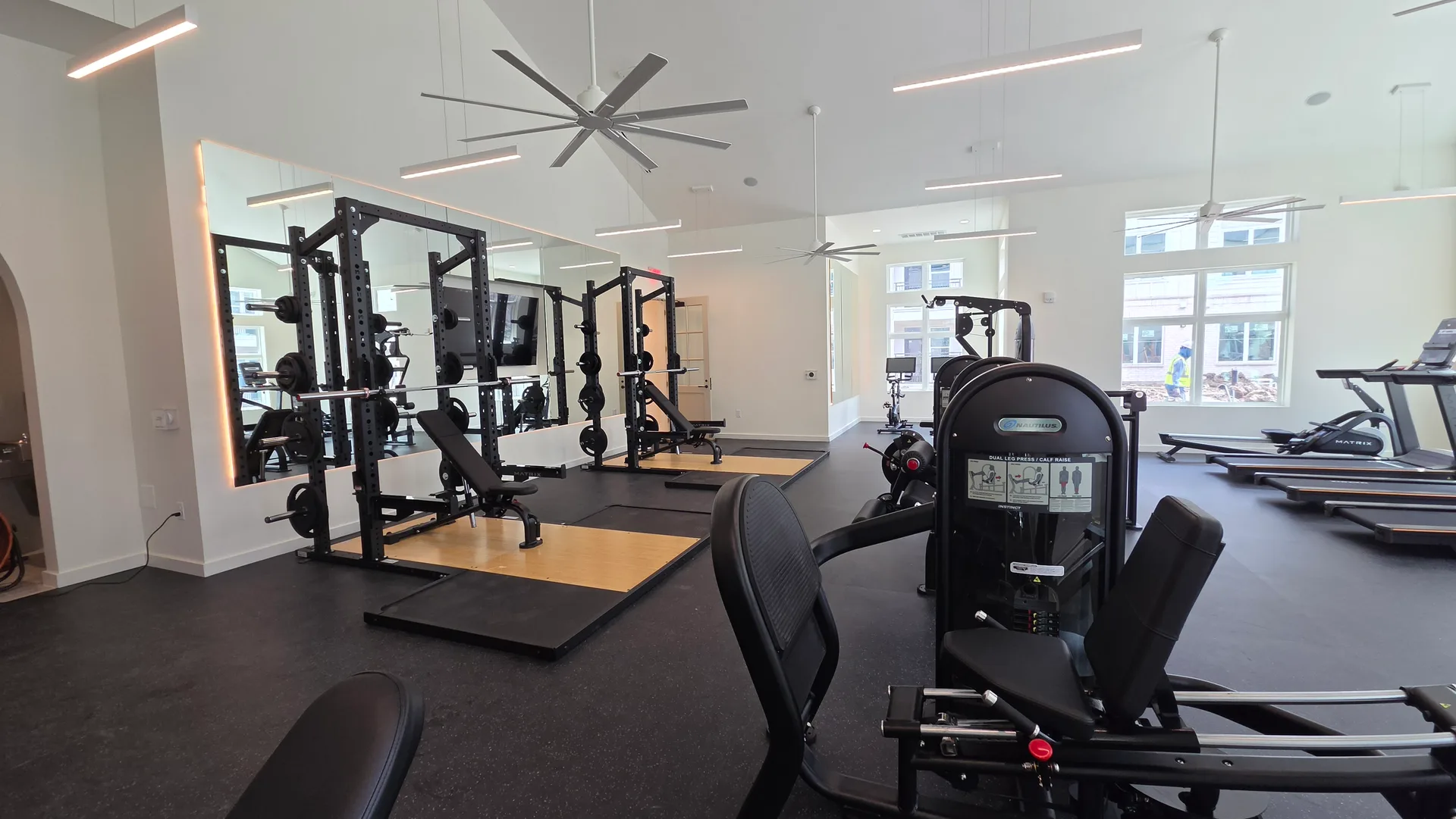Matrix half racks on hardwood-inlay lifting platforms before a backlit mirror in a Webster, Texas apartment gym
