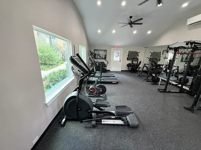 Ellipticals along a window, treadmills and a combination rack system in a vaulted apartment gym in The Woodlands, Texas